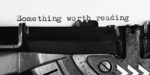 Black and white image of typewriter with paper inserted and typed words 'something worth reading'